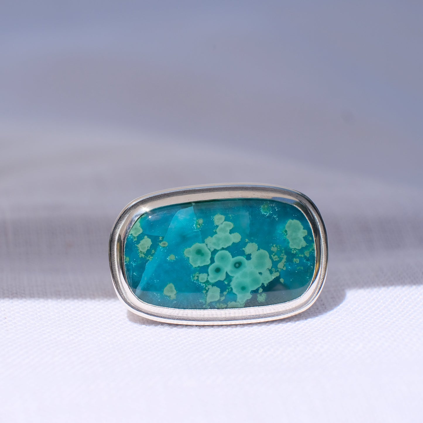 Ring with a blue gemstone on a white and gray gradient background